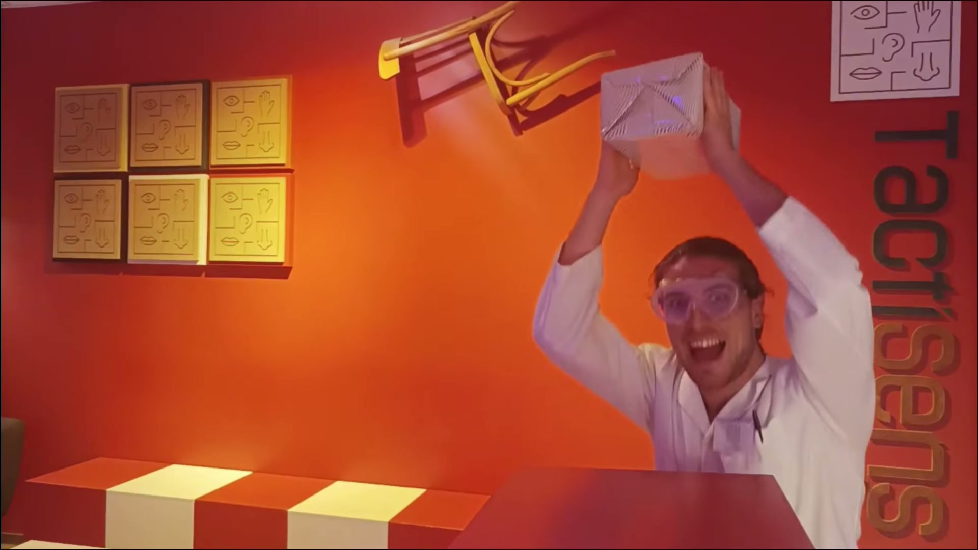 Game Master Tactisens avec un paquet cadeau dans le décor orange, extrait de la vidéo anniversaire