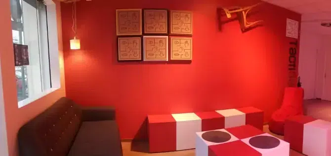 L’espace d’accueil aux murs rouges, avec un canapé et des cubes pour s’asseoir
